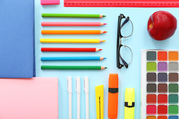 Eyeglasses with fresh red apple and different stationery on blue background