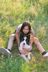 Girl spending time with a black and white Border Collie dog outdoors on a sunny day, sitting and...
