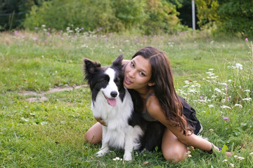 Girl spending time with a black and white Border Collie dog outdoors on a sunny day, sitting and...