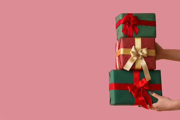 Female hands holding Christmas gift boxes on pink background