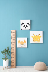 Wooden stadiometer with cute animal paintings and houseplant near blue wall