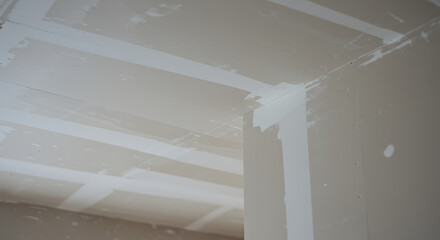 Unfinished drywall seams and joint compound on walls and ceiling during interior construction and renovation.
