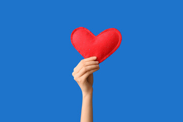 Female hand holding decorative heart on blue background