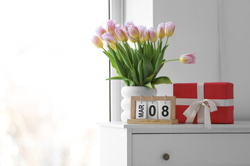 Calendar with date of International Women's Day, tulips and gift box on commode in bedroom