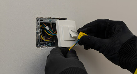 Electrician's gloved hands wiring a light switch during home electrical installation or repair