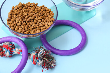 Bowl with dry food and chew toys on blue background
