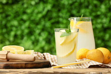 Glass and jug of fresh lemonade with mint on wooden table outdoors