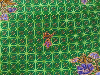 Colorful batik fabric with purple floral patterns, brown leaves, and intricate green geometric...