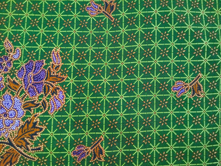 Colorful batik fabric with purple floral patterns, brown leaves, and intricate green geometric...
