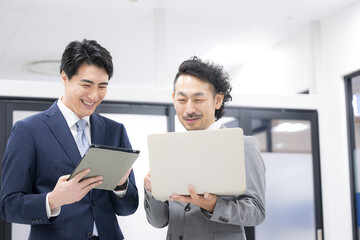 Two businessmen in suits having a meeting while looking at a computer. A boss teaching a new employee and a meeting scene.