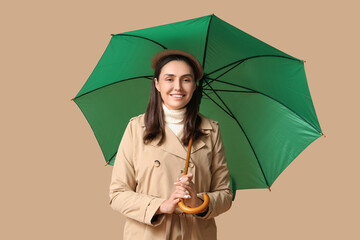 Happy young woman with umbrella on beige background