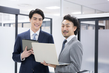 パソコンを見る打ち合わせをするスーツを着たビジネスマン2人　新人さんに教える上司や打ち合わせの様子　カメラ目線