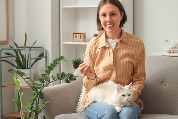 Young woman with cat and anti-parasitic spot-on applicator sitting on sofa at home