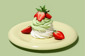 Plate of sweet Pavlova cake with fresh strawberries and mint on green background