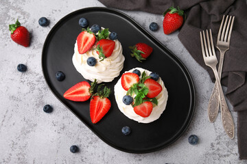 Plate of sweet Pavlova cakes with fresh berries and mint on grey background