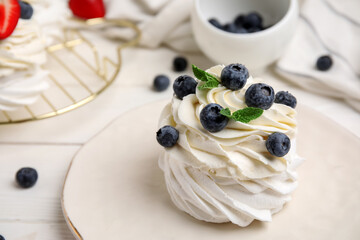 Plate of sweet Pavlova cake with fresh blueberries and mint on white wooden background, closeup