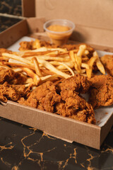 Close-up view of fried chicken with French fries in a cardboard box ready for delivery.
