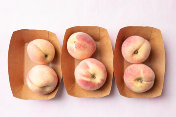 Top view of fresh peaches in paper bowl on pink background, Summer fruit