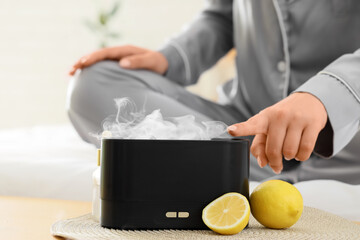 Young woman with air humidifier and lemons on table in bedroom, closeup