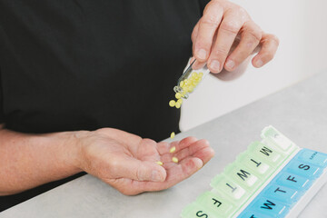An elderly woman pours yellow pills out of a bottle into a container.