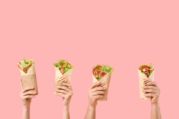 Hands with tasty sandwich wraps on pink background