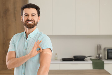 Young man with applied medical patch showing OK after vaccination in kitchen