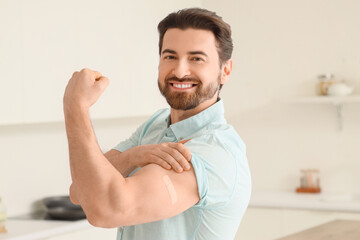 Young man with applied medical patch showing muscles after vaccination in kitchen