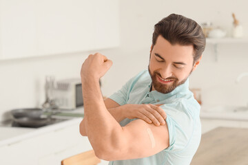 Young man with applied medical patch showing muscles after vaccination in kitchen