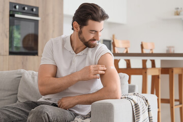 Young man with applied medical patch on sofa after vaccination in kitchen
