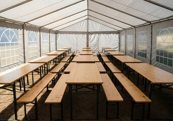 Oktoberfest Rows of wooden picnic tables and benches set up inside a white event tent with arched windows