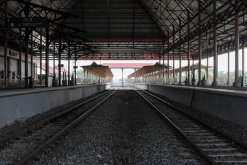 View of an empty railway station platform with parallel tracks and structural metal roofing