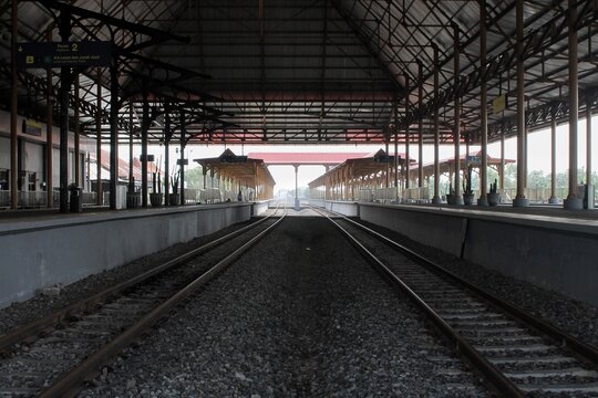 View of an empty railway station platform with parallel tracks and structural metal roofing