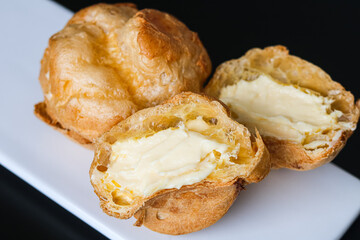 Two freshly baked Kue Sus (Choux Pastries or Cream Puffs), with one cut in half to show the fluffy cream filling inside.