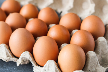 Closeup of fresh brown eggs nestled in a rustic, textured paper egg carton. The warm, earthy tones of the eggs highlight concepts of natural food, healthy ingredients, and sustainable packaging.