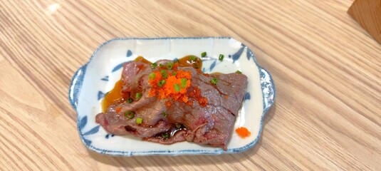 Wagyu beef sushi topped with tobiko and Japanese green onions, placed on a ceramic tray.