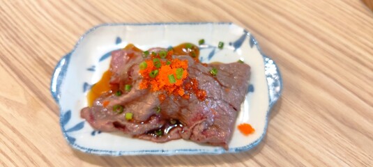 Wagyu beef sushi topped with tobiko and Japanese green onions, placed on a ceramic tray.
