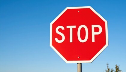 Obraz premium Bright red octagonal stop sign against a clear blue sky.
