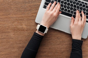 Cropped view of girl with smartwatch typing on laptop keyboard on wooden background