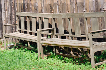 Two old weathered wooden benches sit side by side in a grassy yard next to a rustic wooden fence
