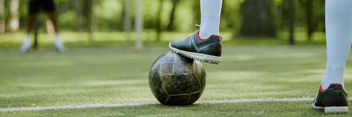 Header of teenager standing on soccer field placing foot on soccer ball, wearing athletic shoes and...