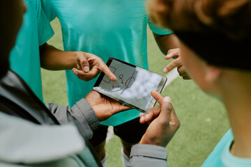 Group of teenage boys discussing sports strategy while pointing at digital tablet displaying play...