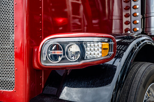 Front part of the red big rig classic semi truck with chrome details and black fenders with shiny reflective surface