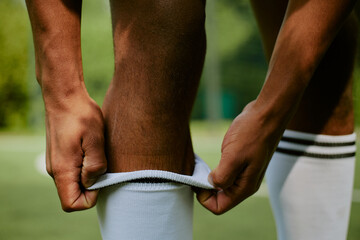 Man adjusting long athletic socks on lower legs outdoors, preparing for sports activity on green...