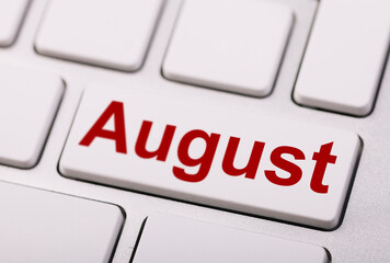 Close-up of a white computer keyboard with a red "August" key, representing time, scheduling, or monthly planning in a digital context.