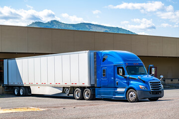 Long hauler blue big rig semi truck with dry van semi trailer loading cargo standing in warehouse dock