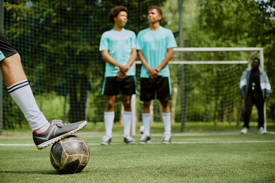 Teenage boy preparing to kick soccer ball during free kick while two teenage boys, one Black and one Caucasian, standing in defensive wall on outdoor soccer field - Powered by Adobe