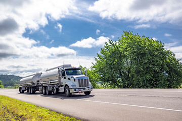 White day cab powerful big rig semi truck transporting liquid cargo in two tank semi trailer...