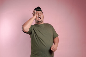 A man in a green shirt is screaming. The man is wearing a hat and has his hands on his head