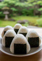 A plate of Japanese onigiri, rice balls, with seaweed topping, in a garden setting.