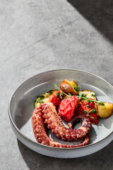 Grilled octopus plated with roasted potatoes and vegetables, bright lighting, overhead composition